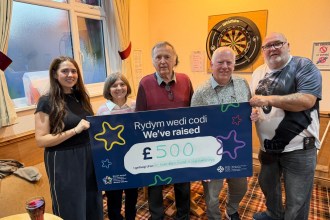 Five people holding a large Swansea Bay Health Charity cheque for £500 in front of a dartboard at Pontarddulais Conservative Club