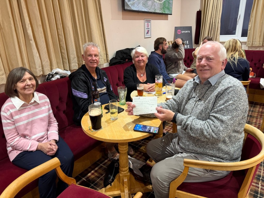 Four quiz regulars at a round table in Pontarddulais Conservative Club, one holding up a cheque