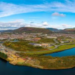 Aerial view of the Port Talbot waterfront at Harbourside, with industrial yards and scrubland beside the water and the town and hills behind.