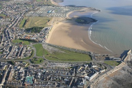 Aerial view of Porthcawl seafront, with the town in the foreground, the harbour on the right and a wide sandy beach curving away towards caravans in the distance