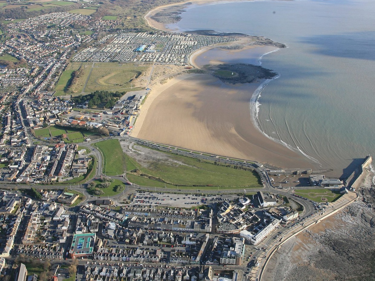 Aerial view of Porthcawl seafront, with the town in the foreground, the harbour on the right and a wide sandy beach curving away towards caravans in the distance