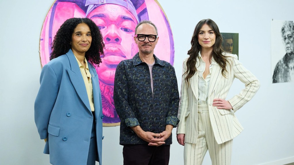 Two women and a man in glasses standing in a white gallery in front of a large round pink and purple portrait painting