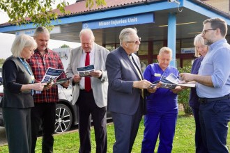 Seven people reading draft leaflets outside the Minor Injuries Unit entrance at Prince Philip Hospital in Llanelli, including SOSPPAN campaigners, a Llais representative and nursing staff in blue uniforms