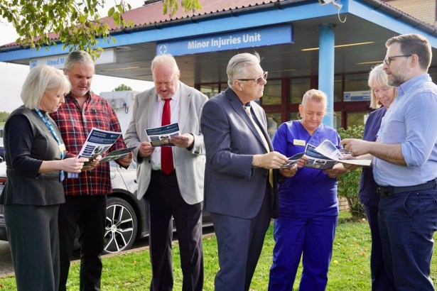 Seven people reading draft leaflets outside the Minor Injuries Unit entrance at Prince Philip Hospital in Llanelli, including SOSPPAN campaigners, a Llais representative and nursing staff in blue uniforms