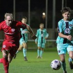 Afan Lido's Alex Giardelli in red and Pure Swansea's Harvey Chapman in the teal away kit chasing the ball under the floodlights