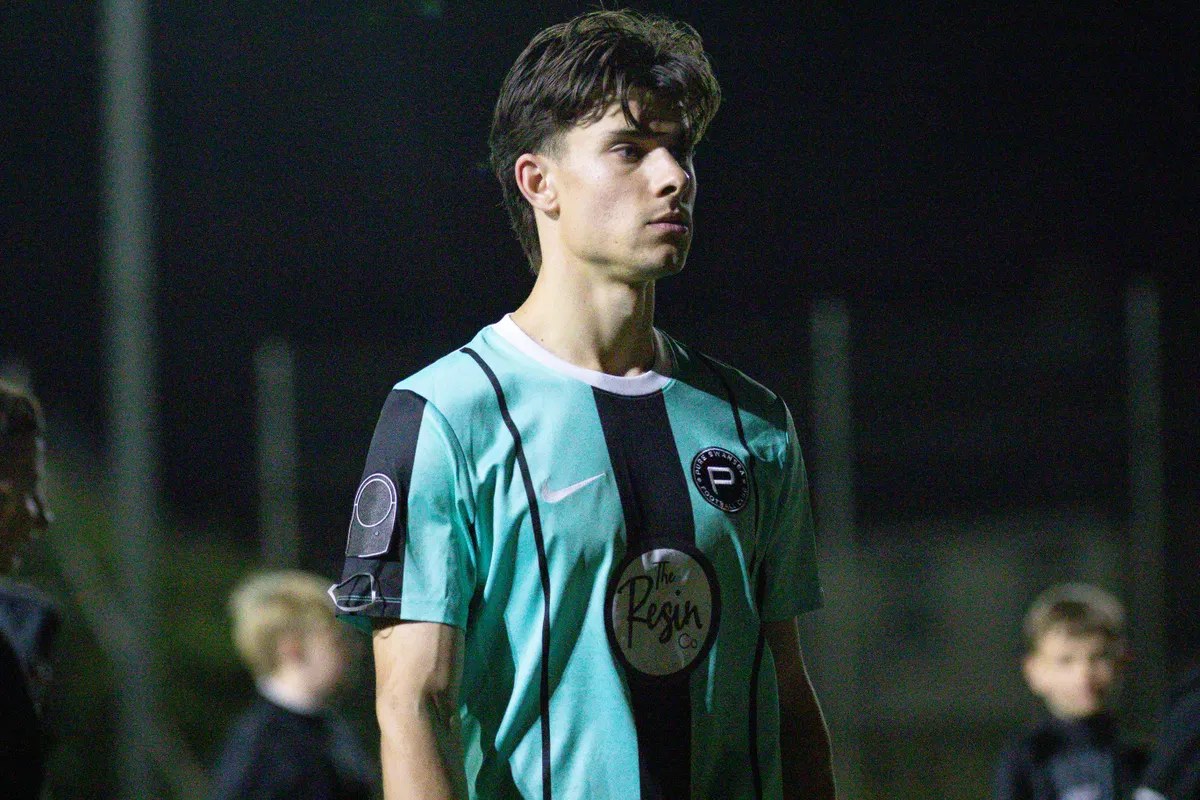 Pure Swansea's Jacob Lund in the turquoise and black striped home kit, looking across the pitch under the floodlights