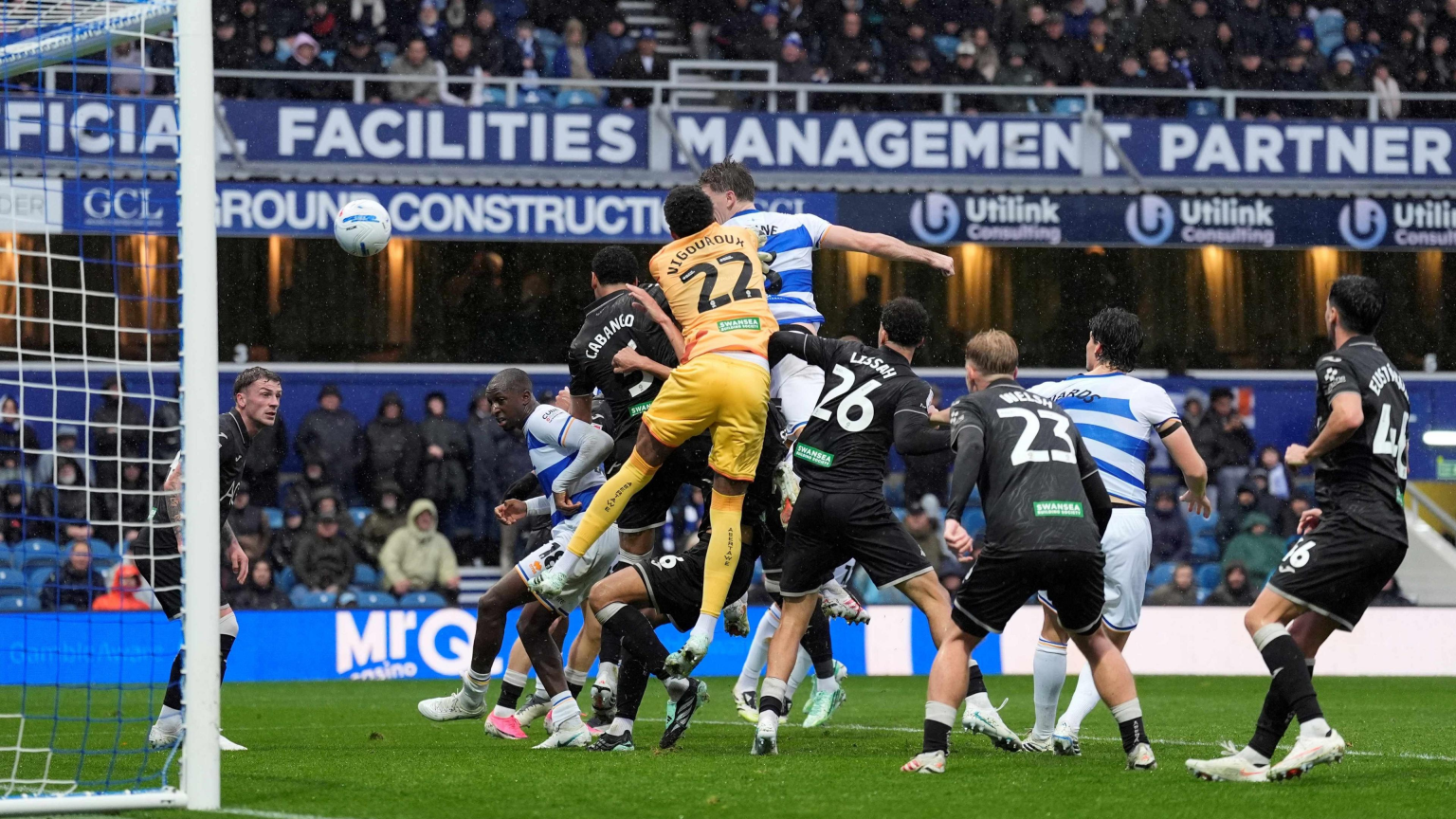 QPR defender Jimmy Dunne heads the ball over Swansea City goalkeeper Lawrence Vigouroux in a crowded penalty area at Loftus Road.