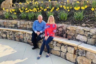 Cllr Richard Lewis and his daughter Francesca O'Brien sitting on a stone-filled gabion wall in front of a bank of daffodils