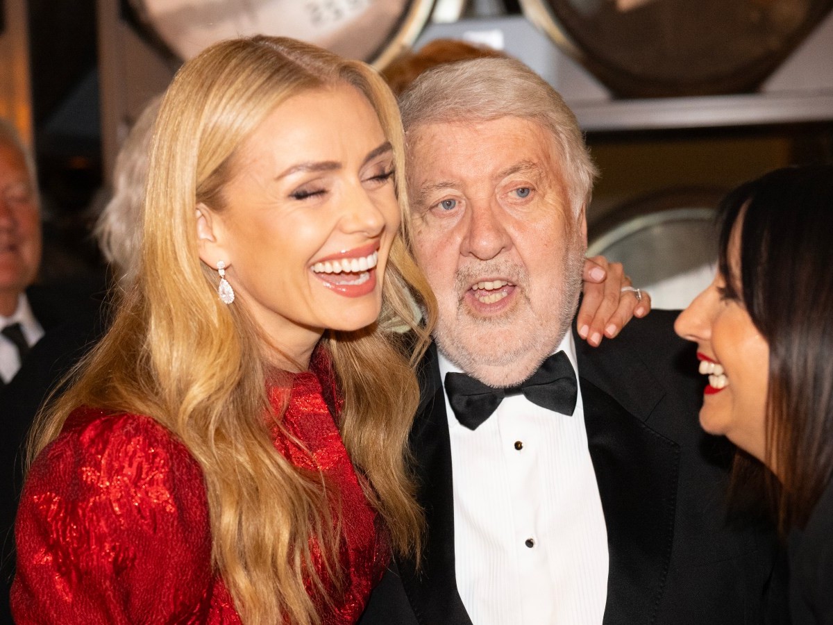 Roy Noble in a dinner jacket laughing with Katherine Jenkins and Lucy Owen in front of whisky barrels