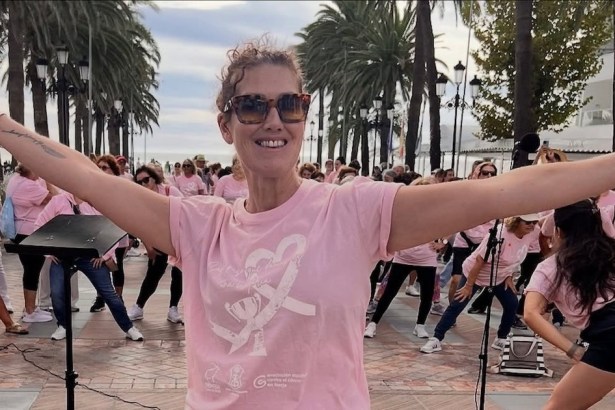 Sam Ward-Jones in a pink T-shirt and sunglasses, smiling with her arms outstretched in front of a crowd of people in matching pink T-shirts