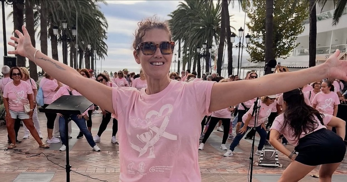 Sam Ward-Jones in a pink T-shirt and sunglasses, smiling with her arms outstretched in front of a crowd of people in matching pink T-shirts