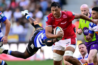 Scarlets lock Sam Lousi, in red, carries the ball through a tackle from a Stormers player in blue and white hoops.