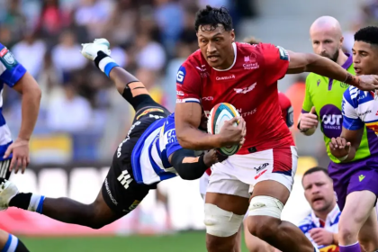 Scarlets lock Sam Lousi, in red, carries the ball through a tackle from a Stormers player in blue and white hoops.