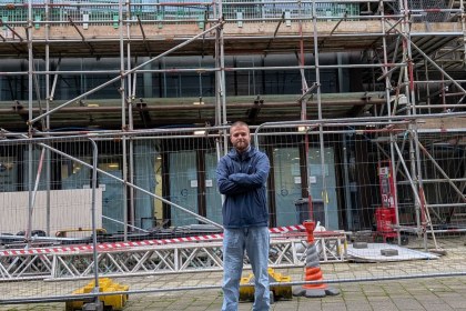 Scott Bayes standing with arms folded in front of security fencing and scaffolding on the former Debenhams building in Carmarthen