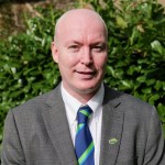 Cllr Scott Jones, the new leader of Neath Port Talbot Council, in a grey jacket and blue and green striped tie in front of a laurel hedge