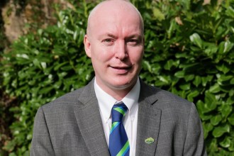 Cllr Scott Jones, the new leader of Neath Port Talbot Council, in a grey jacket and blue and green striped tie in front of a laurel hedge