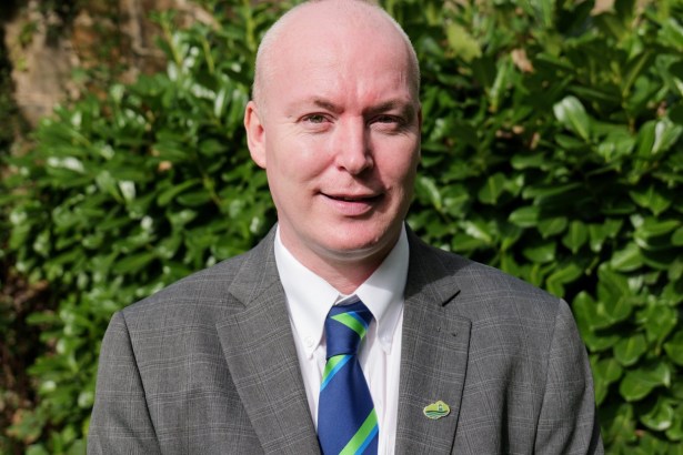 Cllr Scott Jones, the new leader of Neath Port Talbot Council, in a grey jacket and blue and green striped tie in front of a laurel hedge
