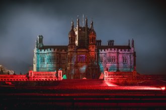 Margam Castle at night, lit in red, blue and pink, with red light across the stone steps in front