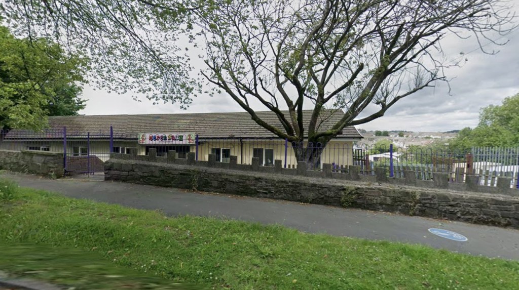A single-storey nursery building behind a stone wall and purple railings, with a colourful Seren Fach sign above the entrance