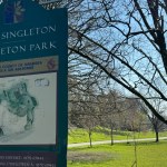 The bilingual Parc Singleton / Singleton Park sign with a City and County of Swansea crest and park map, with trees and lawns behind