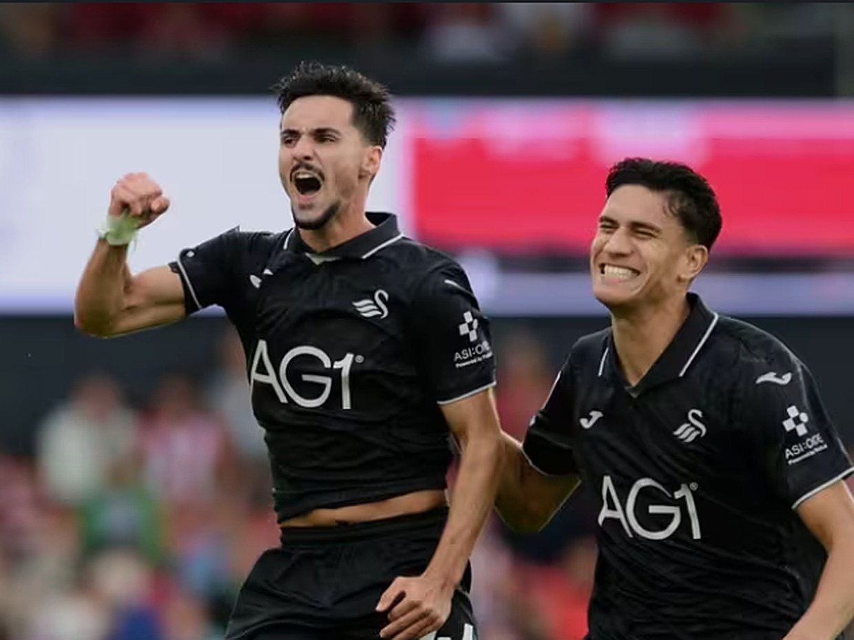 Swansea City midfielder Stephen Eustáquio, in the black away kit, shouting and clenching his fist in celebration as team-mate Marko Stamenic runs alongside
