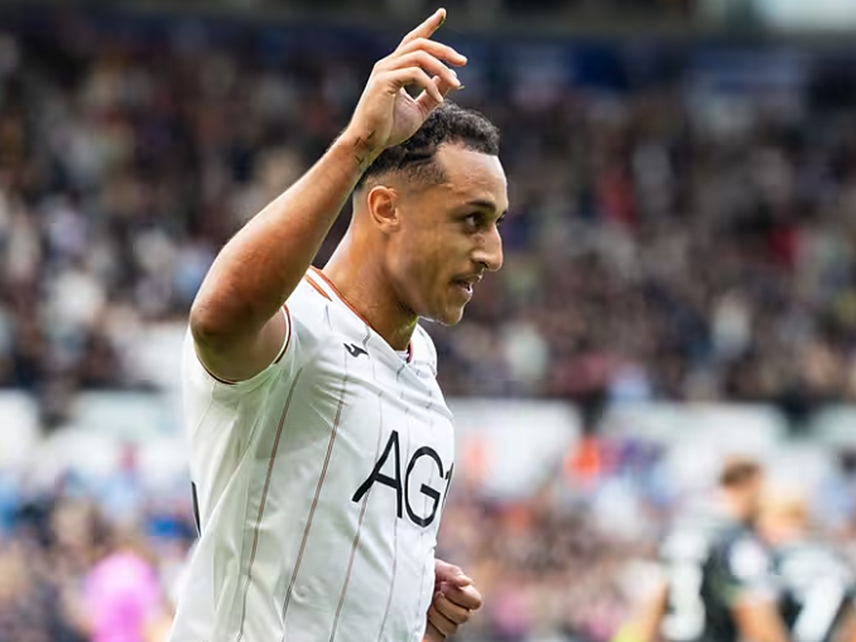 Swansea City striker Adam Idah, in a white home shirt, raises a hand to celebrate in front of the crowd at the Swansea.com Stadium