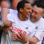 Scott Sinclair, smiling, is embraced by team-mate Stephen Dobbie as they celebrate in Swansea City's white kit