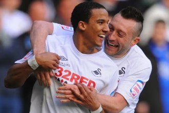 Scott Sinclair, smiling, is embraced by team-mate Stephen Dobbie as they celebrate in Swansea City's white kit