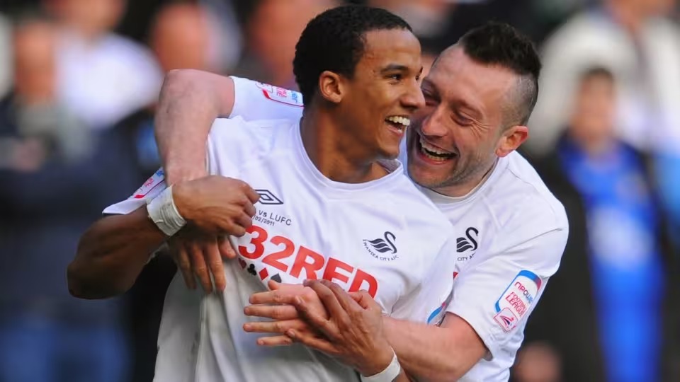 Scott Sinclair, smiling, is embraced by team-mate Stephen Dobbie as they celebrate in Swansea City's white kit