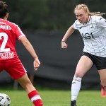 A Swansea City Women player in the white home kit runs at a Wrexham defender in red at the ThermaGlaze Ground in Garden Village