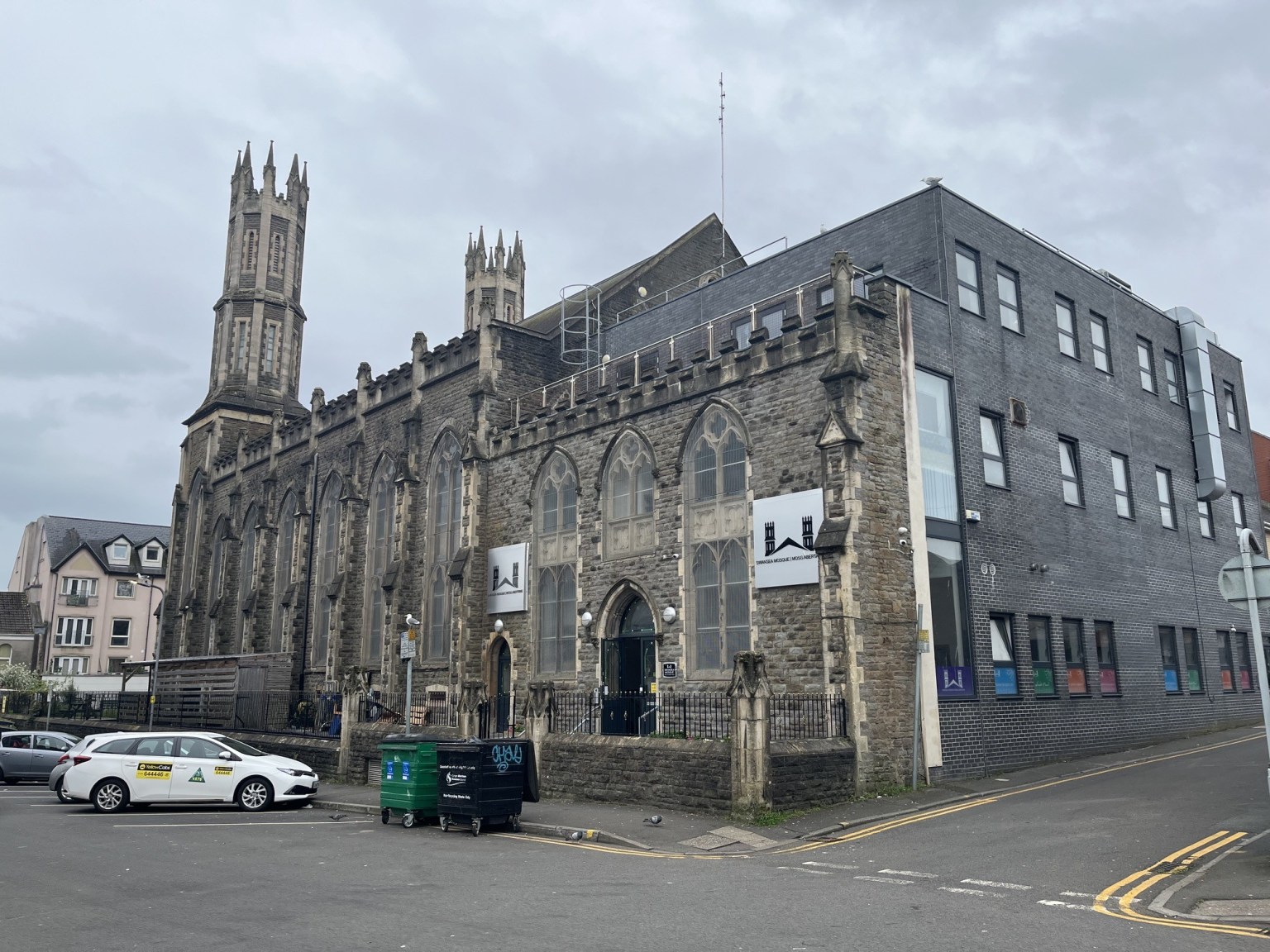 The Gothic stone building of Swansea Mosque and Islamic Community Centre with its tall pinnacled tower and a modern grey extension