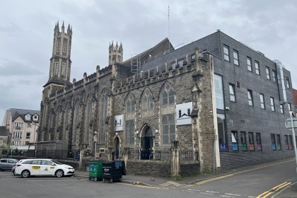 The Gothic stone building of Swansea Mosque and Islamic Community Centre with its tall pinnacled tower and a modern grey extension