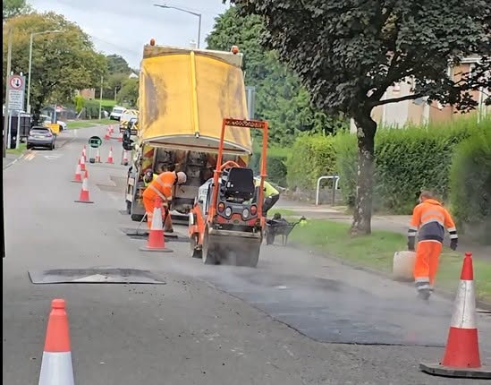 Swansea Council highways crew in orange hi-vis with a roller and cones repairing a stretch of residential road