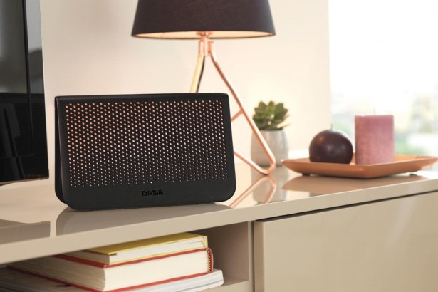 A black TalkTalk broadband router on a living room sideboard beside a television and a table lamp