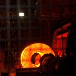 A glowing orange coil of hot steel on a mill, with sparks falling around it