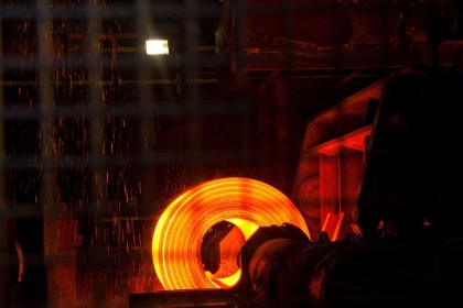 A glowing orange coil of hot steel on a mill, with sparks falling around it