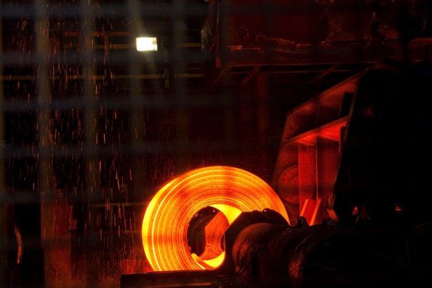 A glowing orange coil of hot steel on a mill, with sparks falling around it