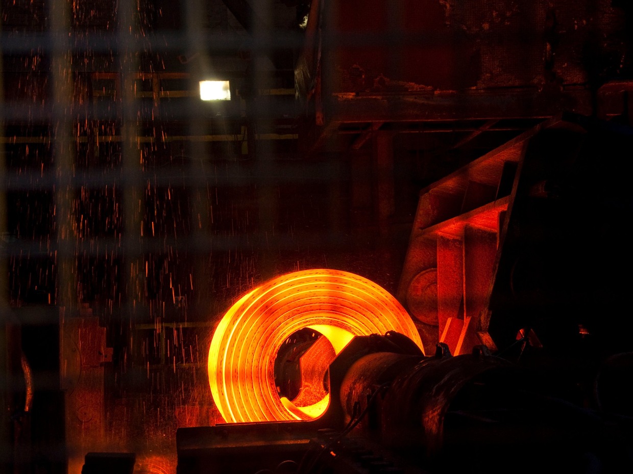 A glowing orange coil of hot steel on a mill, with sparks falling around it