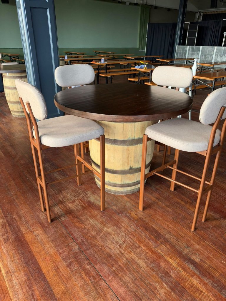 Four tall upholstered stools around a round table built on a wooden barrel, with beer-hall benches behind