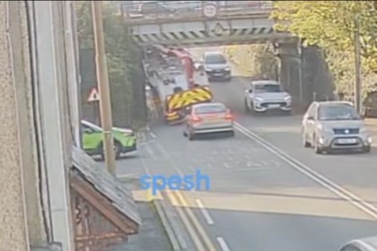 A lorry with a red crane arm under the Trafle Mill railway bridge on Victoria Road, Gowerton, with traffic queuing in both directions