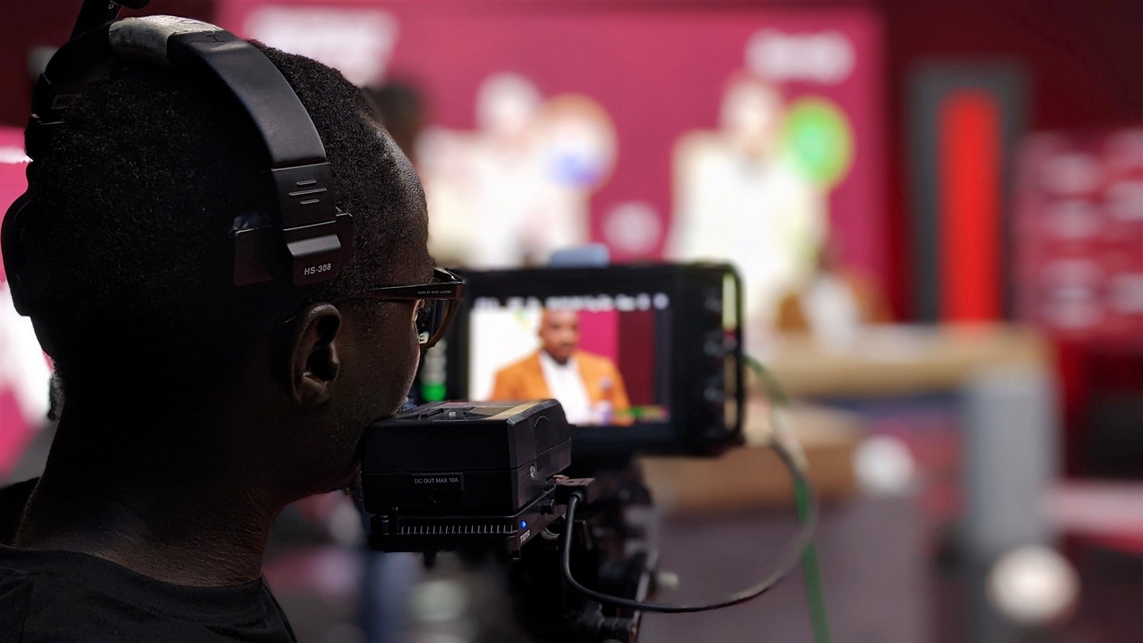 A camera operator wearing headphones films a presenter in a television studio