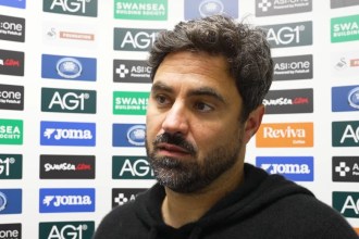 Swansea City head coach Vitor Matos, in a black hoodie, speaking in front of a sponsor board after the game against West Ham