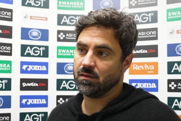 Swansea City head coach Vitor Matos, in a black hoodie, speaking in front of a sponsor board after the game against West Ham