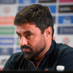 Swansea City head coach Vitor Matos at a press conference, in front of a sponsor board.