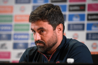 Swansea City head coach Vitor Matos at a press conference, in front of a sponsor board.