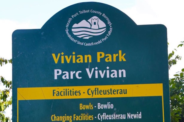 Green Neath Port Talbot County Borough sign reading Vivian Park and Parc Vivian, with a yellow facilities panel listing bowls and changing facilities, against trees and sky.