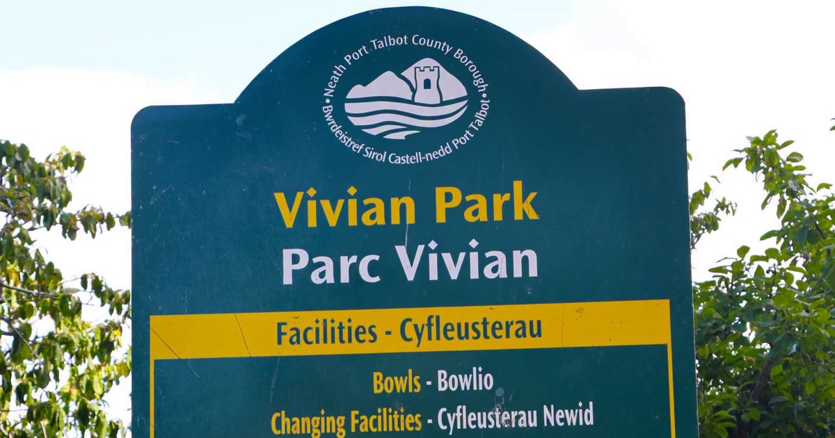Green Neath Port Talbot County Borough sign reading Vivian Park and Parc Vivian, with a yellow facilities panel listing bowls and changing facilities, against trees and sky.