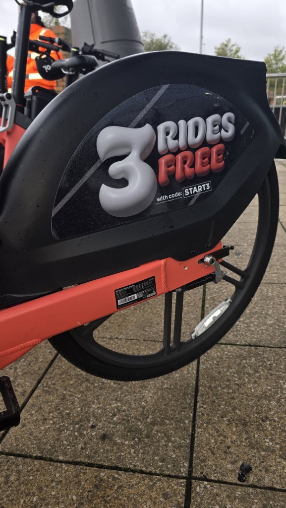 Close-up of a black rear wheel cover on an orange Voi e-bike with a sticker reading 3 rides free with code START3