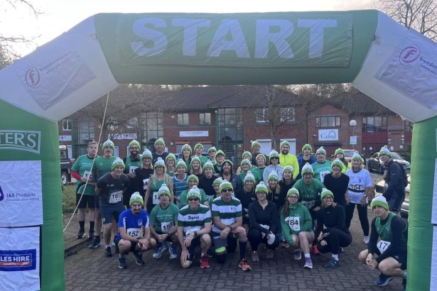 Dozens of runners in green-and-white bobble hats and race numbers posing under an inflatable green START arch