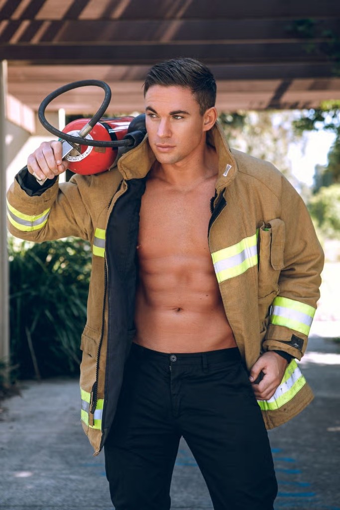 Will Parfitt in an open firefighter’s jacket, carrying a fire extinguisher over his shoulder